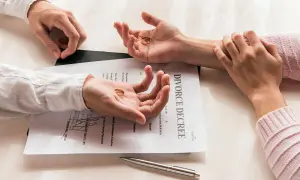 Dwie dłonie trzymają obrączki na tle dokumentu "DIVORCE DECREE". Pozew o rozwód z orzekaniem o winie.