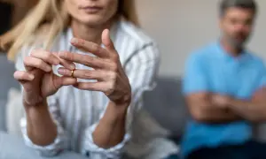 Kobieta zdejmuje obrączkę, symbol końca małżeństwa. W tle siedzi mężczyzna. Wzór pozwu o rozwód z orzeczeniem o winie męża.