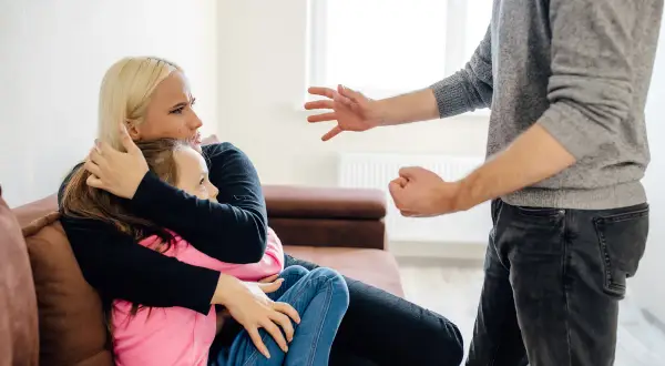 Kobieta chroni córkę przed agresywnym mężczyzną. Groźby karalne mogą prowadzić do poważnych konsekwencji prawnych.
