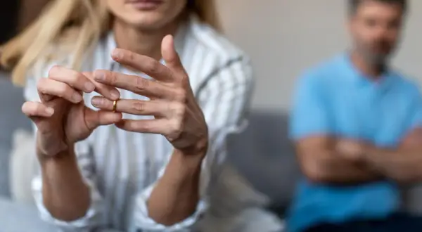 Kobieta zdejmuje obrączkę, symbol końca małżeństwa. W tle siedzi mężczyzna. Wzór pozwu o rozwód z orzeczeniem o winie męża.