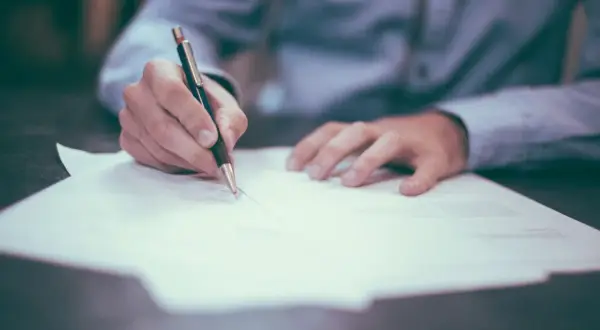 Ręka pisze długopisem na dokumencie. Czy testament można podważyć? Prawnik analizuje dokumenty.