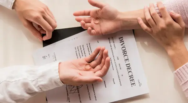 Dwie dłonie trzymają obrączki na tle dokumentu "DIVORCE DECREE". Zastanawiasz się, jak napisać papiery rozwodowe?