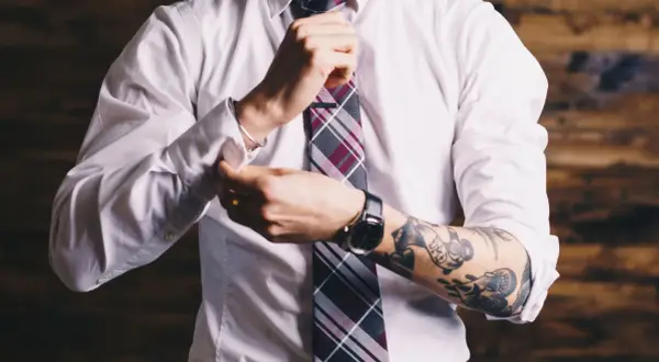 Mężczyzna w białej koszuli i krawacie poprawia mankiet, odsłaniając tatuaż na ramieniu. Czy prawnik może mieć tatuaż? Tak!