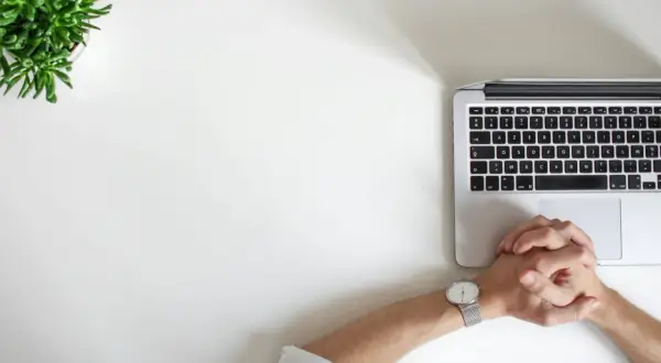Dłonie splecione nad klawiaturą laptopa, obok zielona roślina. Może to być symbol trudnych decyzji, jak rozwód przez internet.