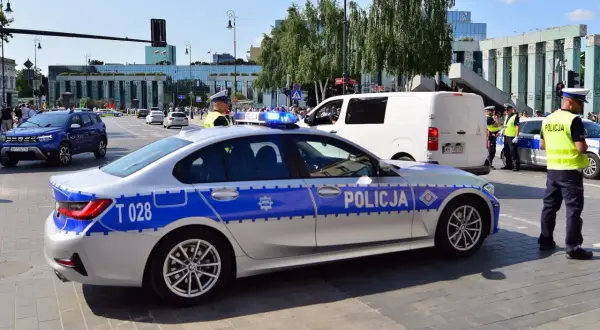 Radiowóz policyjny z włączonymi sygnałami świetlnymi na ulicy, obok policjanci.