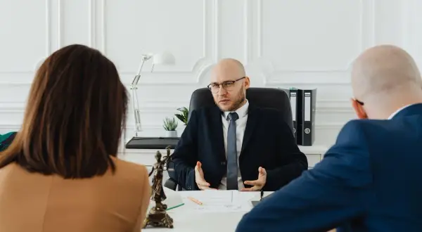 Prawnik wyjaśnia parze, jak napisać wniosek o rozwód. Na stole widać figurkę Temidy.