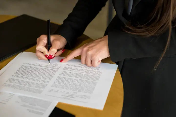 Kobieta z czerwonymi paznokciami podpisuje dokument, który może być wnioskiem o zmianę w księdze wieczystej.